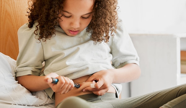 A young girl with diabetes injects an insulin pen into her stomach.