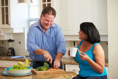 A man and woman talking in a kitchen while cutting up vegetables.