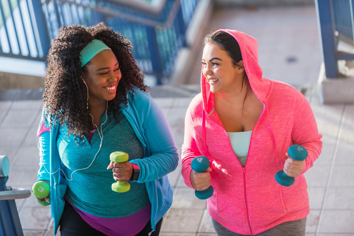 Two women holding dumbbells while jogging up a set of stairs.