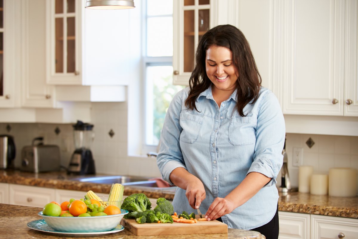 A woman cutting up vegetables in a kitchen.