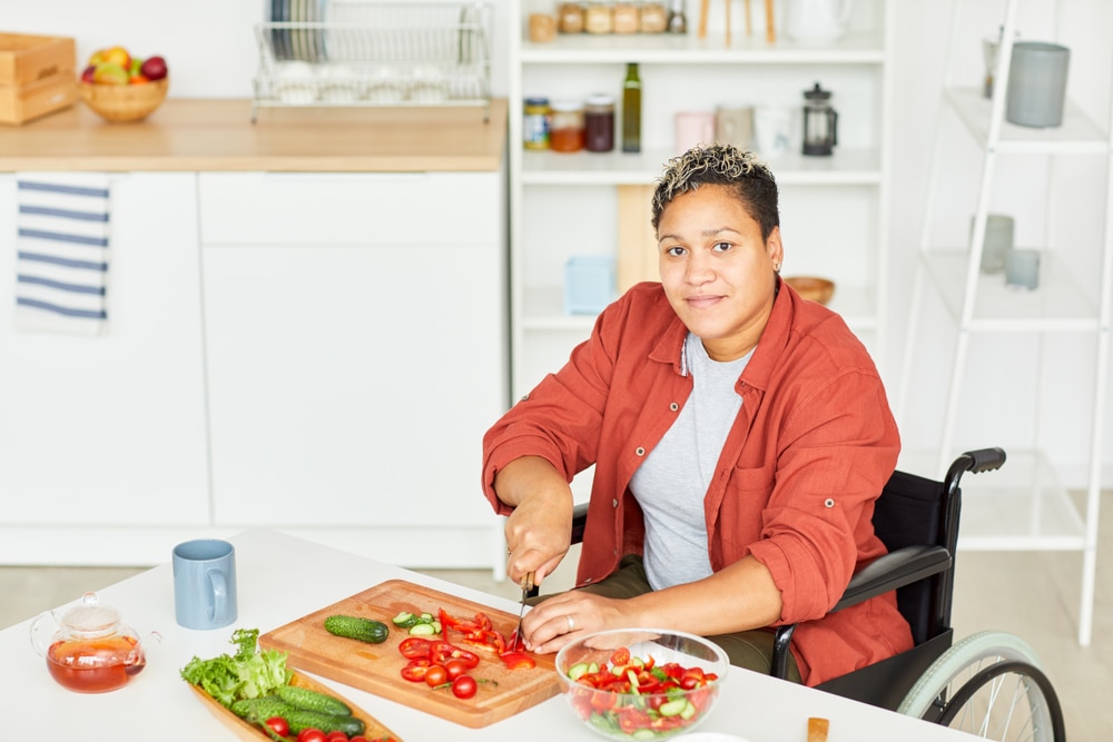 Una mujer en silla de ruedas pica vegetales en la mesa de la cocina.