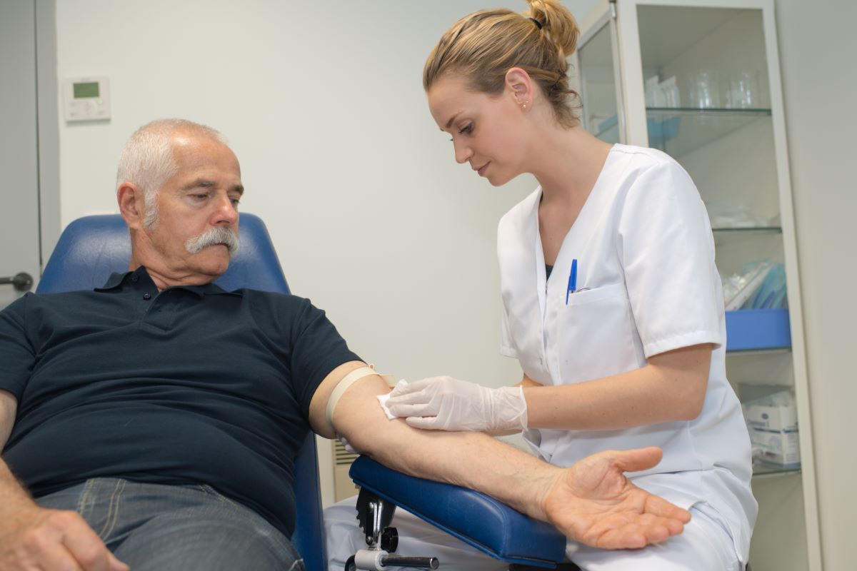 A female health care professional draws blood from a male patient.