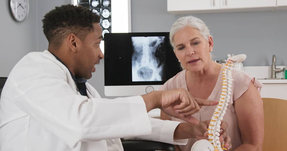 A health care professional shows a spinal model to a woman.