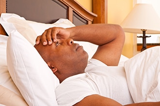 A man lying in bed, holding his forehead.