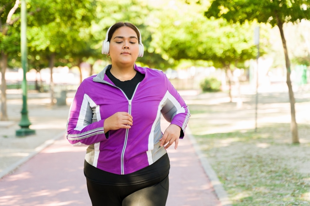 A young woman wearing headphones goes for a run at the park.