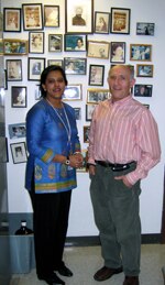 Photo of Rina and Paul in front of a wall with photos of past lab members