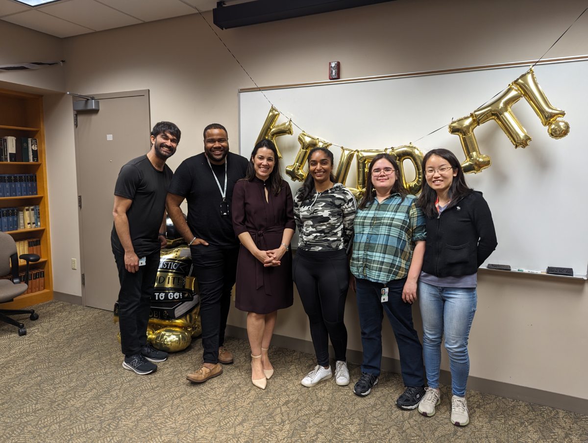 A group of people standing and smiling in front of gold balloons.